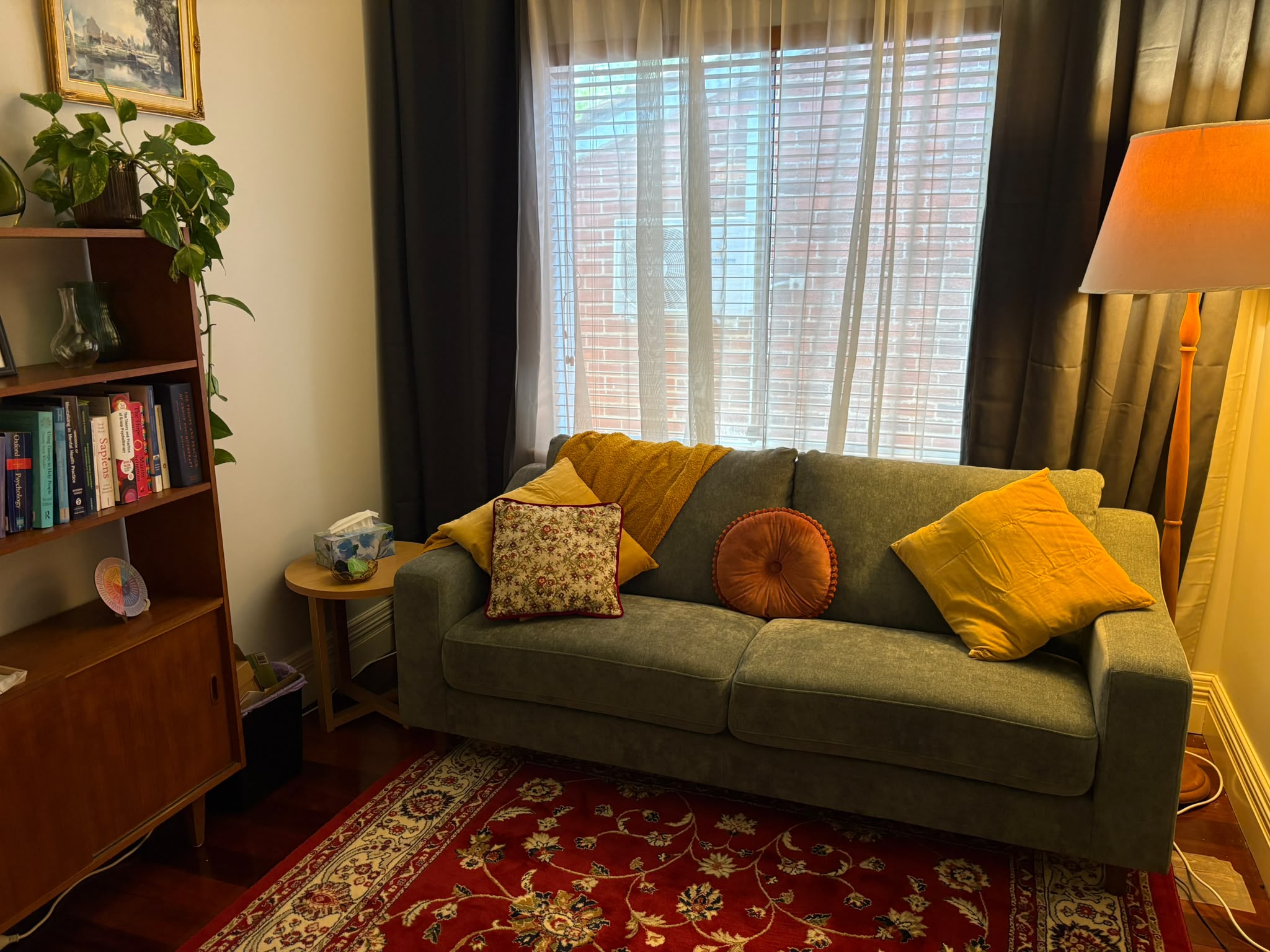 The therapy room: a green sofa by the window with a floor lamp and bookshelf